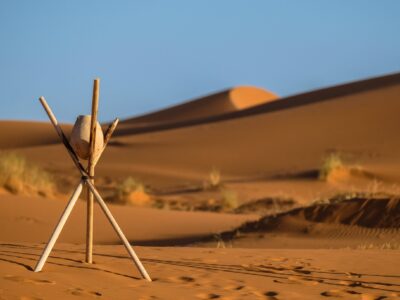 A closeup shot of a rock on a stick tripod with blurred sand dunes in the background