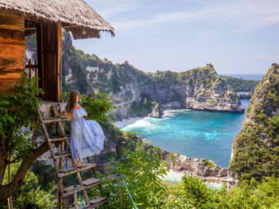 Happy woman standing near tree house at viewpoint Thousand Island. Travel destination in Bali, Indonesia. Popular place to visit on Nusa Penida island.
