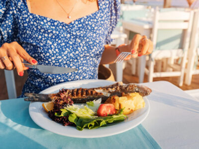 Happy woman with baked sea bass fish in a seafood restaurant. The Mediterranean diet is an indispensable source of omega-3 fats and vitamins