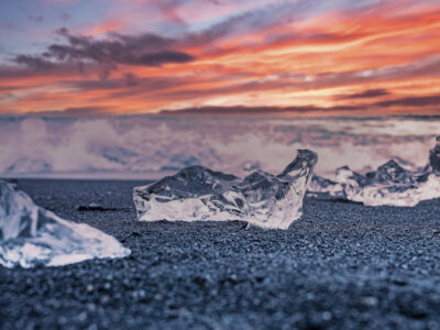 Close-up of iceberg on black sand shore at Diamond beach during sunset. Chunk of floating ice from Jokulsarlon glacier lagoon. View of waves rushing in background against cloudy sky.