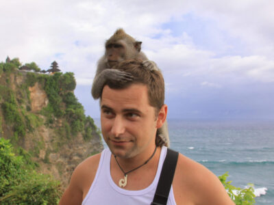 Tourist interacts with macaque monkey on head, at Uluwatu temple, Bali, Indonesia