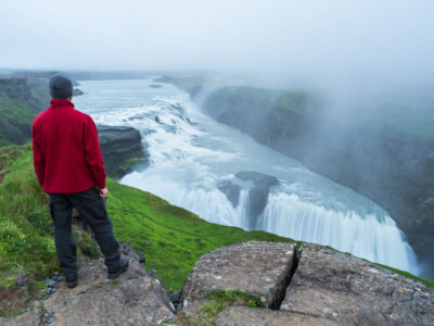 Gullfoss waterfall in the canyon of the mountains. Tourist Attraction Iceland. Man tourist in red jacket stand and looks at the flow of falling water. Beauty in nature