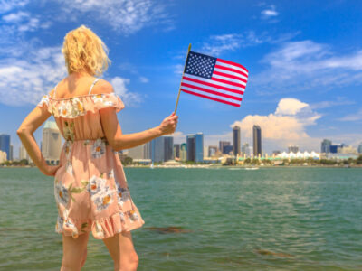 Tourism and travel in California, West Coast, USA. Blonde lady looking San Diego skyline with American flag waving from Coronado Island. Tourist woman in summer holidays. Cityscape in San Diego Bay.