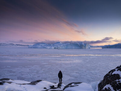 Man watching the sun setting over the frozen sea in Greenland