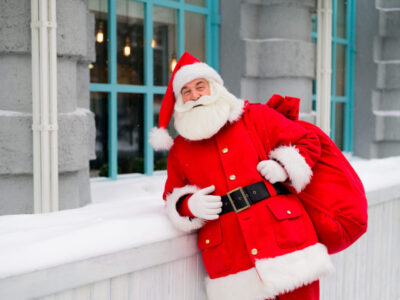 Pensive santa claus is leaning against the facade of a house in winter.