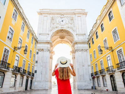 Young woman tourist in red dress standing back in front of the famous triumphal arch in Lisbon city center in Portugal